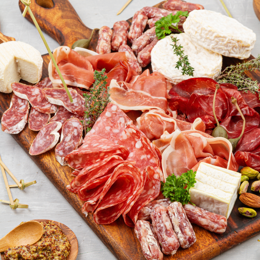 Artisan charcurerie board with selection of cured meat, cheese, olives, crackers all placed on the wooden board on the top of the marble table. Vinesine
