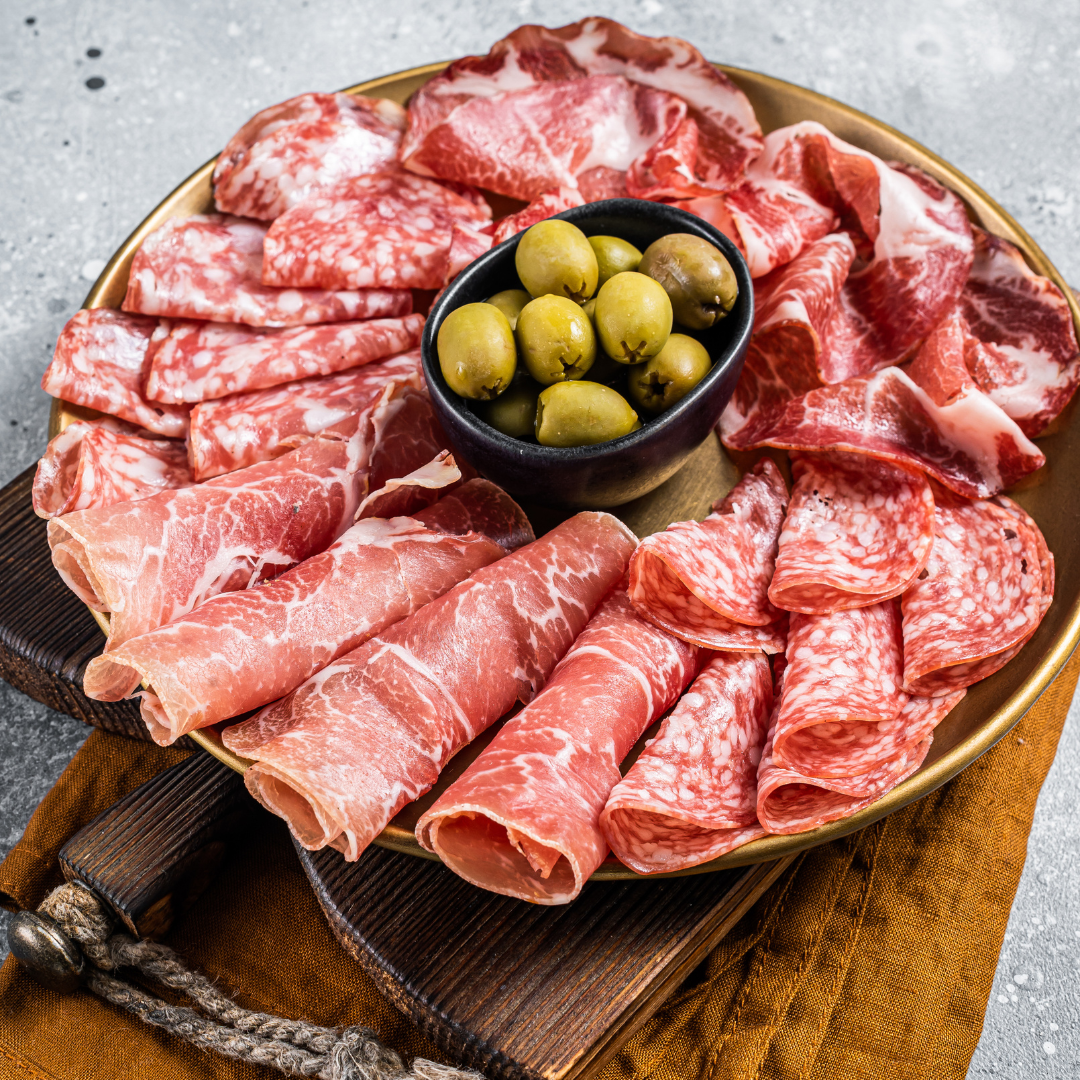 Vinesine offer of selection of cured meat placed on the wooden board with marinated olives in the small black bowl