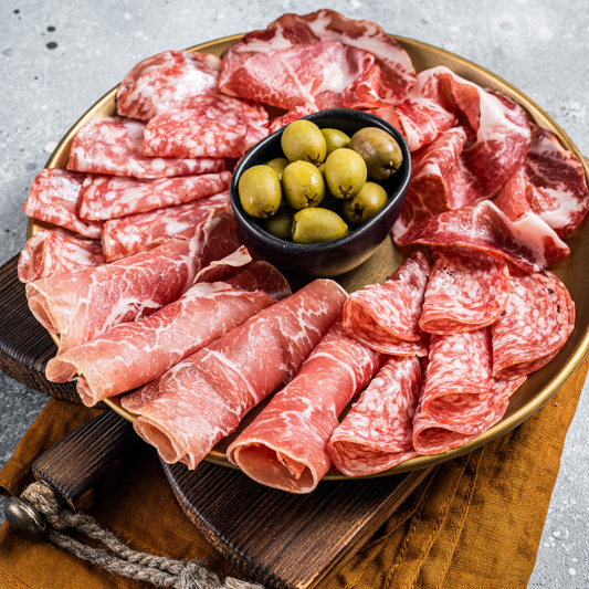 Vinesine offer of selection of cured meat placed on the wooden board with marinated olives in the small black bowl