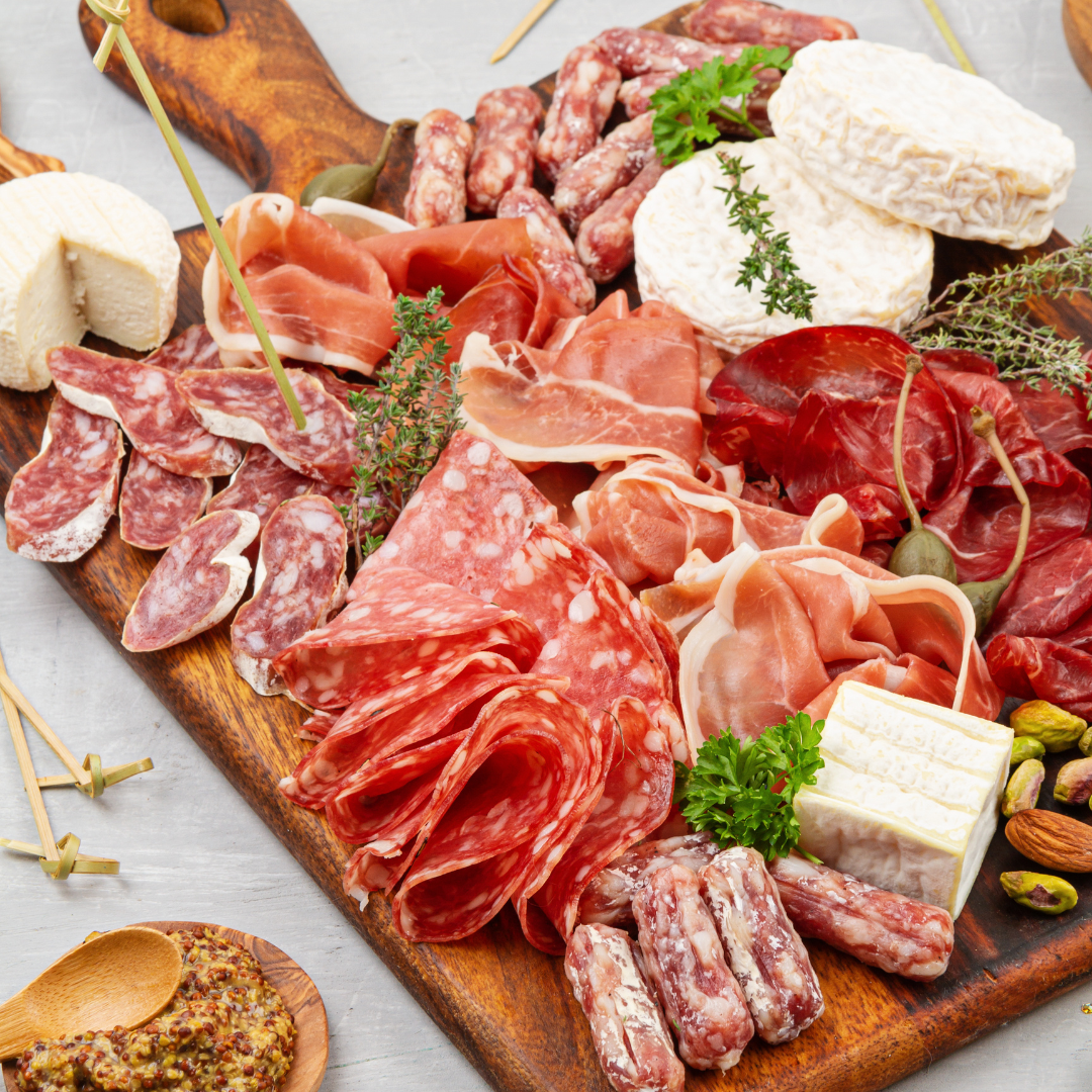 Artisan charcurerie board with selection of cured meat, cheese, olives, crackers all placed on the wooden board on the top of the marble table. Vinesine 